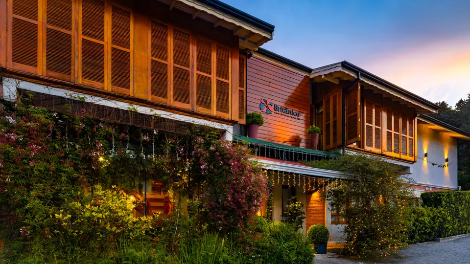 Fachada do Hotel Britânico ao entardecer, com trepadeira florida e luzes acesas na entrada